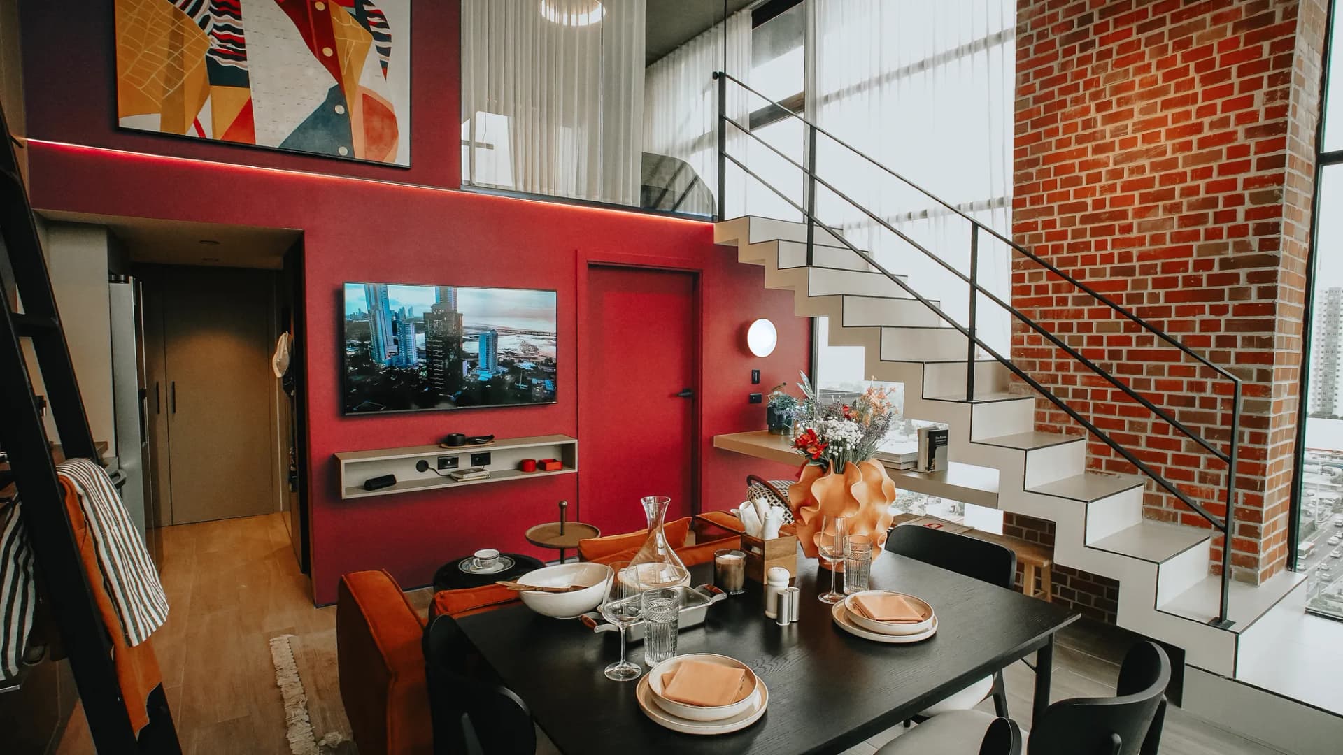 Comedor con muro rojo y escalera en un loft de PH Dovle Cincuentenario